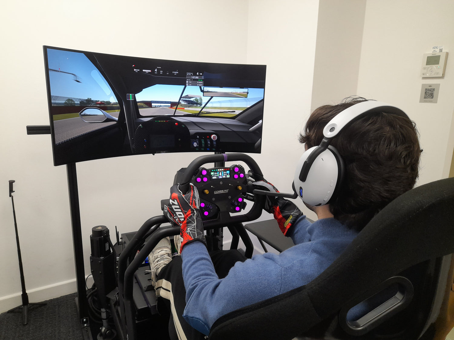Person using a racing simulator with multiple monitors and a steering wheel.