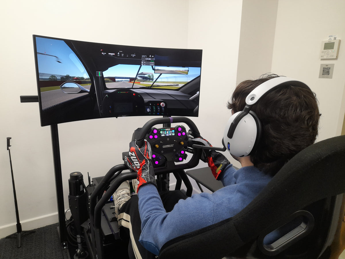 Person using a racing simulator with multiple monitors and a steering wheel.